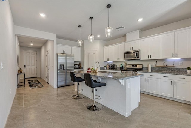 kitchen featuring appliances with stainless steel finishes, a breakfast bar, white cabinetry, dark stone counters, and a center island with sink