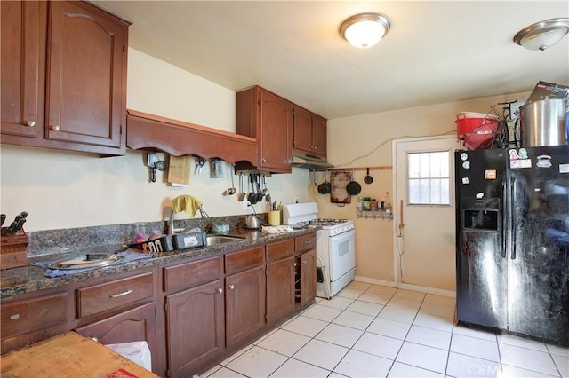 kitchen with sink, dark stone counters, light tile patterned floors, white gas range oven, and black fridge