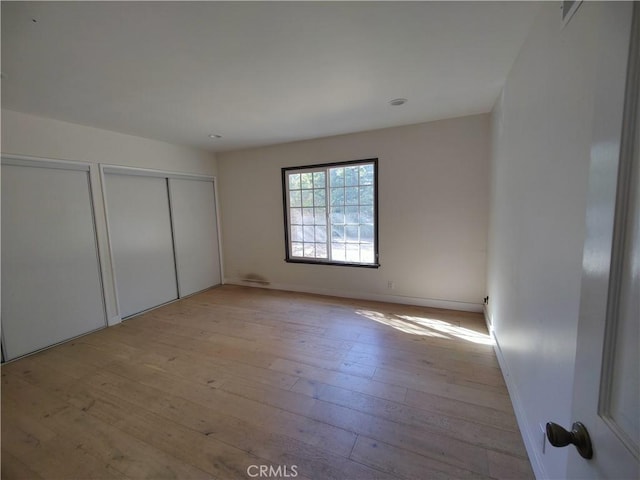 unfurnished bedroom with two closets and light wood-type flooring