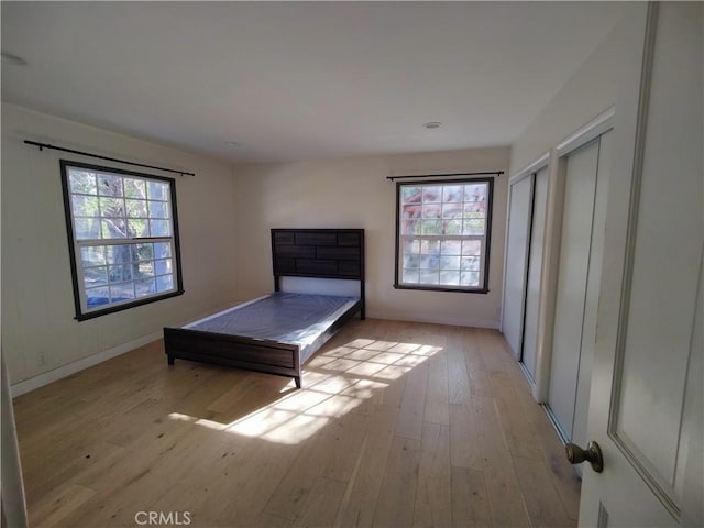 unfurnished bedroom with multiple windows, two closets, and light wood-type flooring