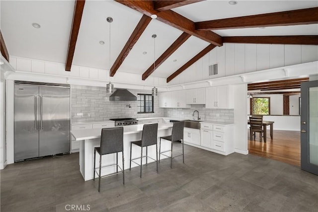 kitchen with range, built in refrigerator, white cabinets, a kitchen island, and wall chimney exhaust hood