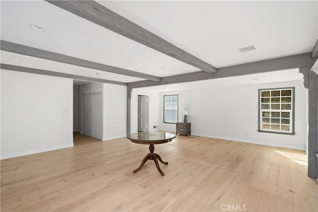 spare room with beam ceiling, light hardwood / wood-style floors, and a wood stove