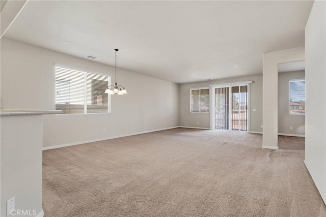 carpeted empty room featuring a wealth of natural light and a chandelier