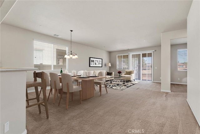 dining space featuring light colored carpet, a healthy amount of sunlight, and a notable chandelier