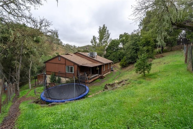 rear view of house featuring a yard, central AC, and a trampoline