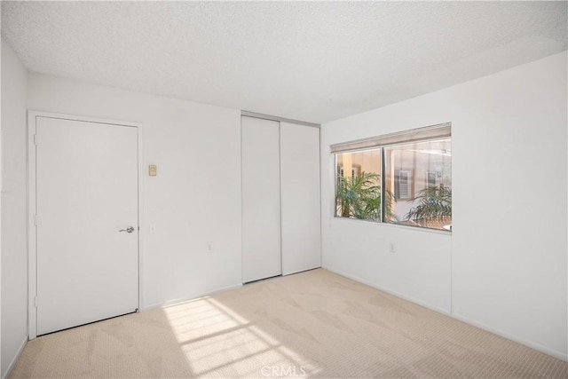 unfurnished bedroom with light colored carpet, a closet, and a textured ceiling