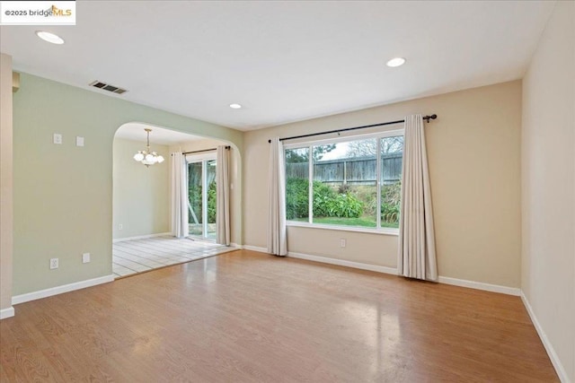 unfurnished room with a notable chandelier and light wood-type flooring