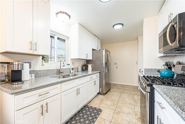 kitchen with sink, light tile patterned floors, appliances with stainless steel finishes, white cabinetry, and light stone counters