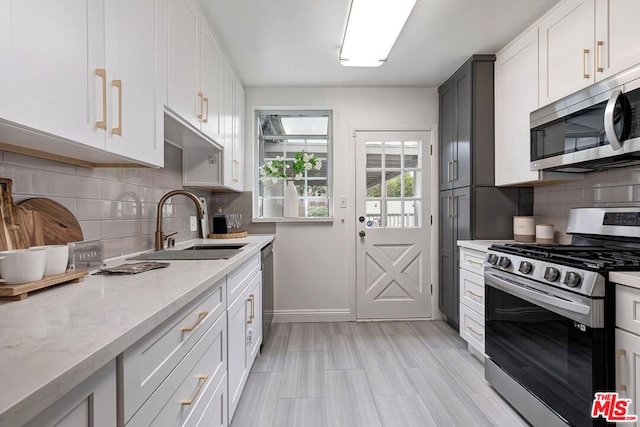 kitchen with white cabinetry, appliances with stainless steel finishes, sink, and light stone counters