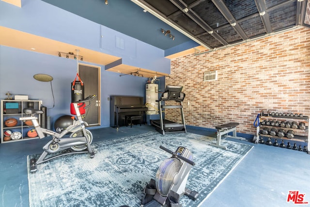 exercise room featuring water heater, brick wall, and a towering ceiling