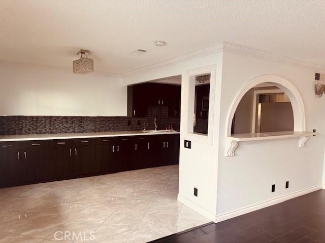 kitchen with dark brown cabinetry, sink, a textured ceiling, stainless steel refrigerator, and backsplash