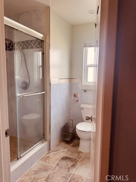 bathroom featuring a shower with door, tile walls, and toilet