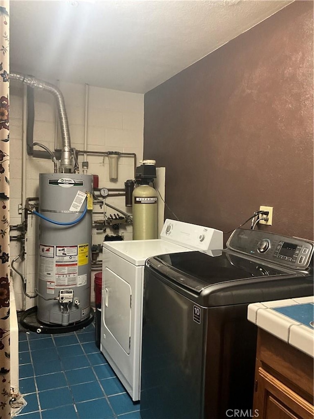 washroom with cabinets, gas water heater, washer and dryer, and dark tile patterned flooring