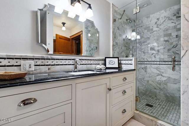 bathroom featuring vanity, a shower with shower door, and decorative backsplash