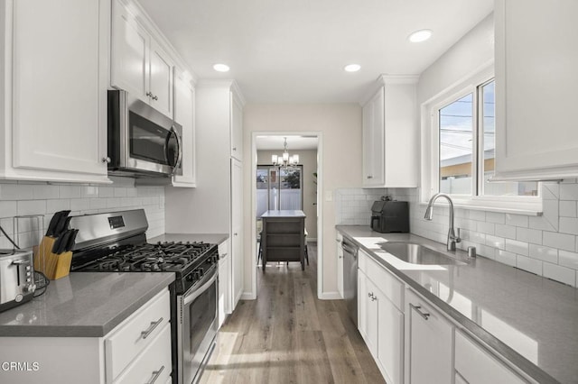 kitchen featuring sink, light hardwood / wood-style flooring, stainless steel appliances, white cabinets, and dark stone counters