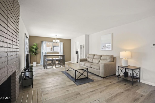 living room with an inviting chandelier, a fireplace, and light hardwood / wood-style floors