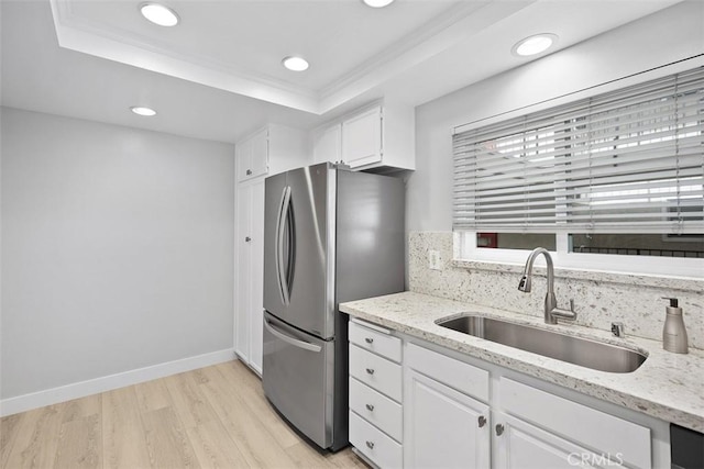 kitchen featuring white cabinetry, sink, stainless steel fridge, a raised ceiling, and light stone countertops