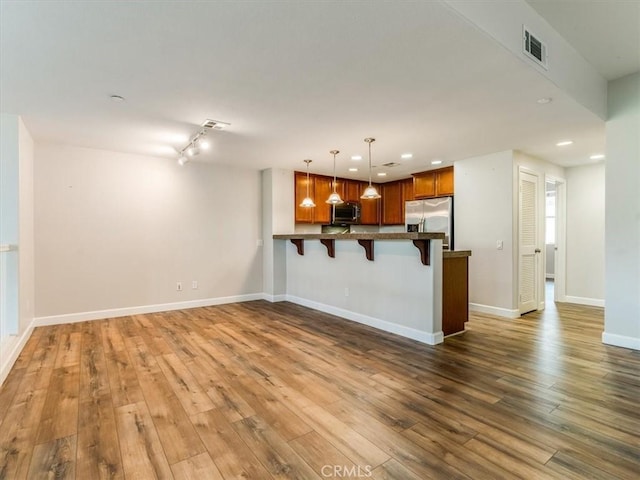 kitchen with visible vents, appliances with stainless steel finishes, a breakfast bar area, wood finished floors, and a peninsula