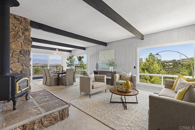 living room with beamed ceiling, a wood stove, a notable chandelier, a mountain view, and a textured ceiling