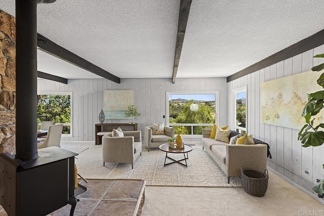 living room with beamed ceiling, carpet flooring, a textured ceiling, and a wood stove