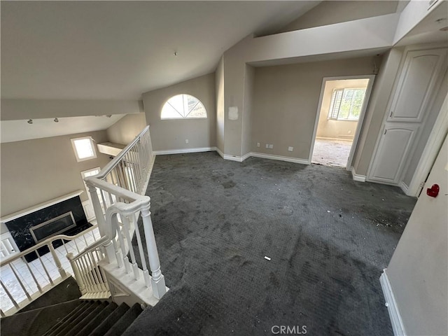 unfurnished living room with vaulted ceiling and dark colored carpet