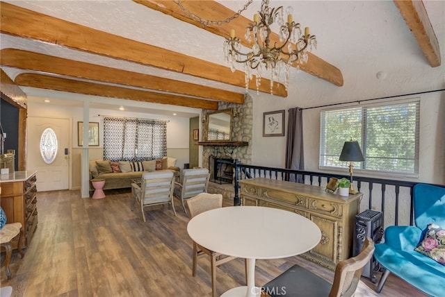 dining room with beamed ceiling, dark hardwood / wood-style floors, an inviting chandelier, and a stone fireplace