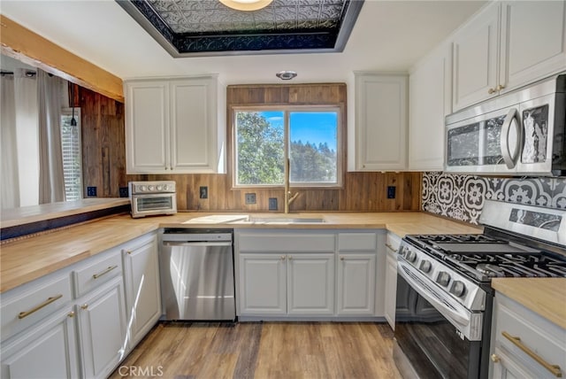 kitchen with a raised ceiling, sink, butcher block counters, white cabinets, and stainless steel appliances