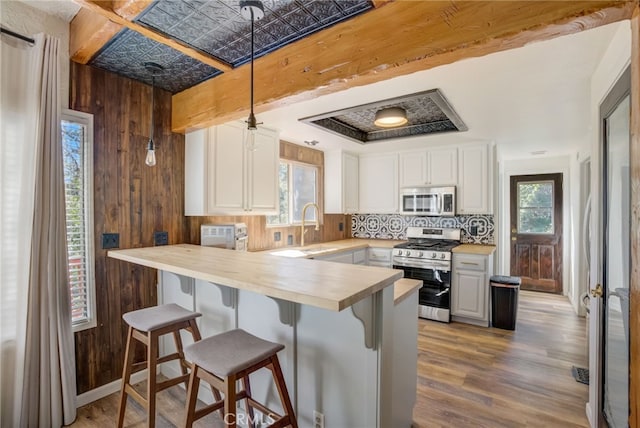 kitchen with appliances with stainless steel finishes, wooden walls, sink, white cabinets, and a kitchen bar