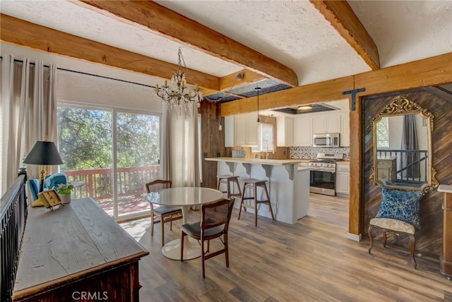 dining space featuring sink, hardwood / wood-style flooring, beam ceiling, a notable chandelier, and a textured ceiling