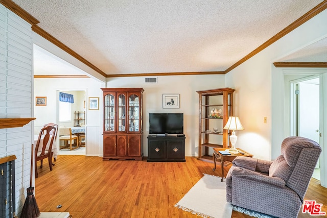 living room with ornamental molding, light hardwood / wood-style floors, a brick fireplace, and a textured ceiling