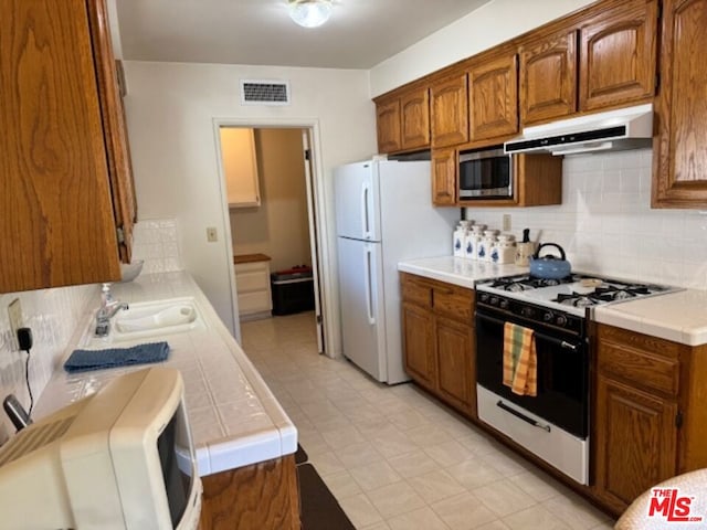 kitchen featuring white refrigerator, gas range, tile countertops, and stainless steel microwave