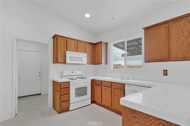 kitchen with lofted ceiling, sink, white appliances, tile countertops, and kitchen peninsula