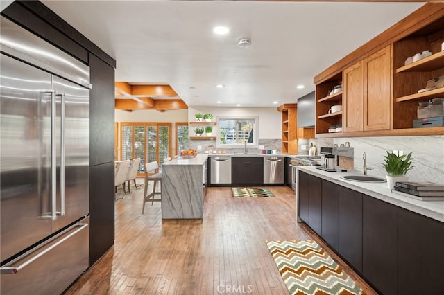 kitchen featuring sink, light wood-type flooring, stainless steel appliances, light stone countertops, and backsplash