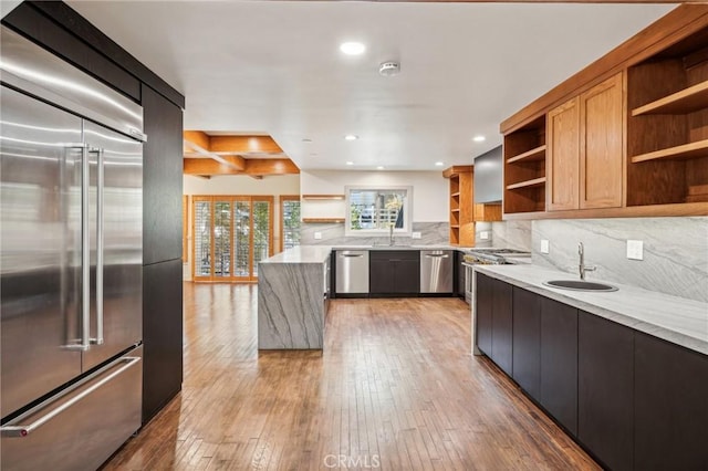 kitchen with sink, tasteful backsplash, high quality appliances, hardwood / wood-style flooring, and light stone countertops