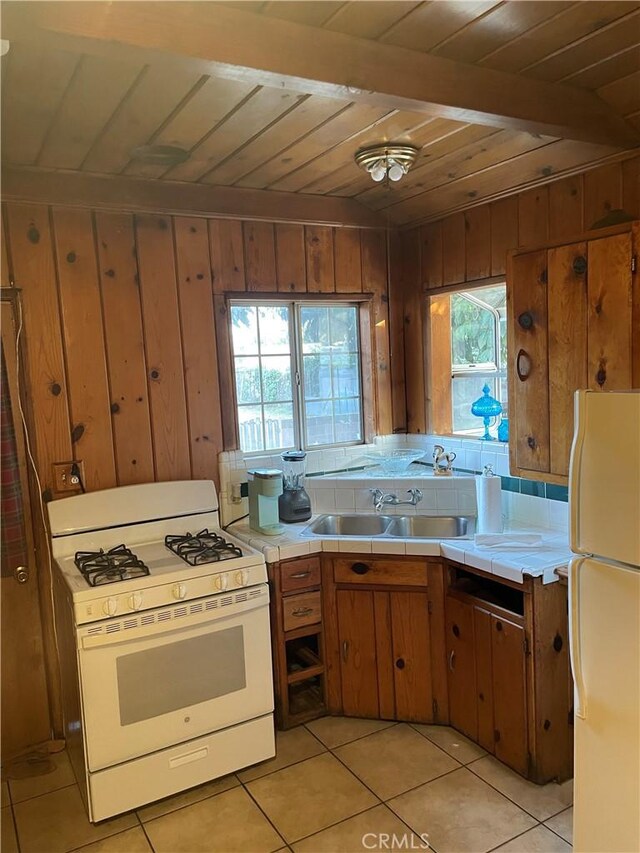 kitchen featuring tile countertops, wood walls, sink, wood ceiling, and white appliances