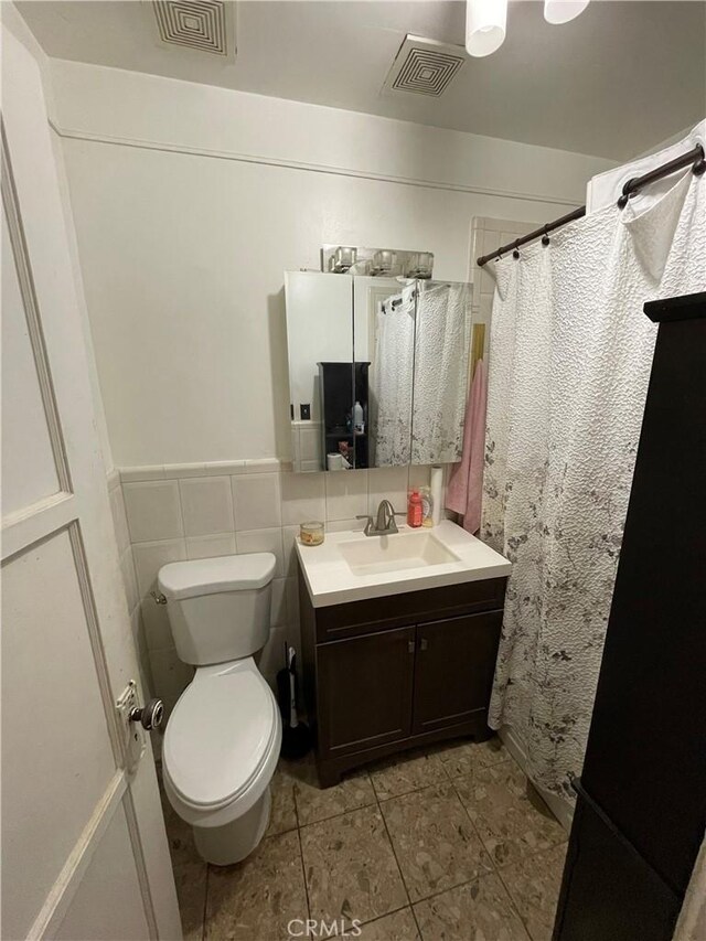 bathroom with tile patterned floors, vanity, toilet, and tile walls