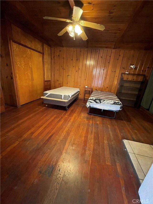 unfurnished bedroom with dark wood-type flooring, wooden ceiling, ceiling fan, and wood walls