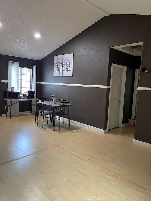 dining space with lofted ceiling, hardwood / wood-style flooring, and a textured ceiling