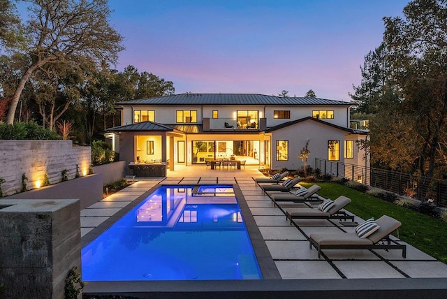 back house at dusk with a fenced in pool, a patio area, and a balcony