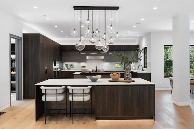 kitchen with decorative light fixtures, an island with sink, dark brown cabinets, and backsplash