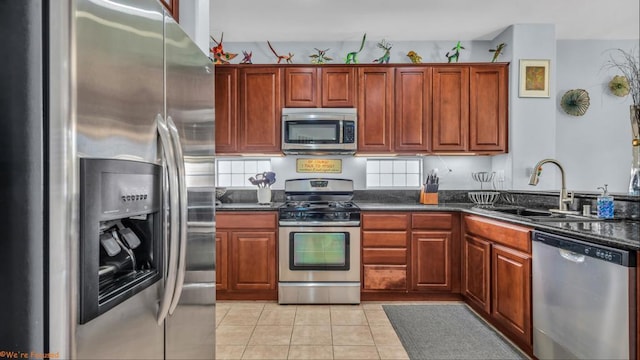 kitchen with stainless steel appliances, sink, dark stone countertops, and light tile patterned floors