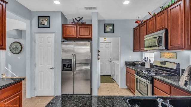 kitchen featuring appliances with stainless steel finishes, light tile patterned floors, and dark stone counters