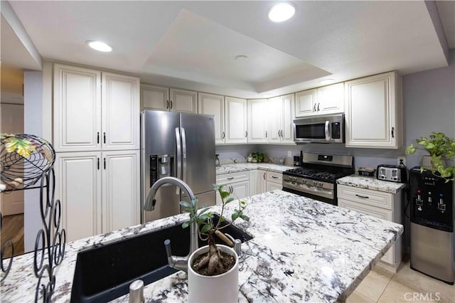 kitchen with sink, light tile patterned floors, appliances with stainless steel finishes, a raised ceiling, and light stone countertops