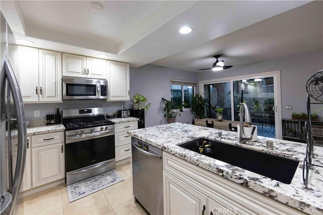 kitchen featuring sink, light stone counters, light tile patterned floors, appliances with stainless steel finishes, and a tray ceiling