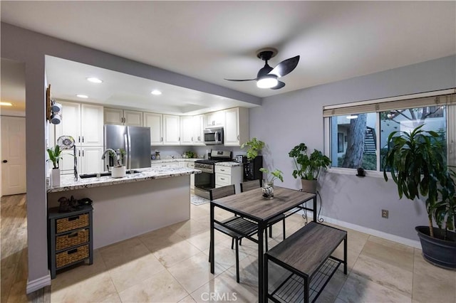 kitchen featuring sink, appliances with stainless steel finishes, kitchen peninsula, light stone countertops, and white cabinets