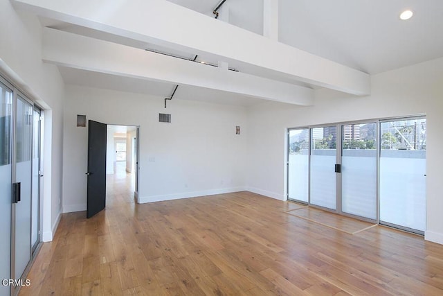 spare room with a towering ceiling, light hardwood / wood-style floors, and beamed ceiling