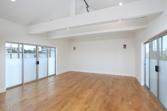 empty room featuring beamed ceiling, light wood-type flooring, and a wealth of natural light