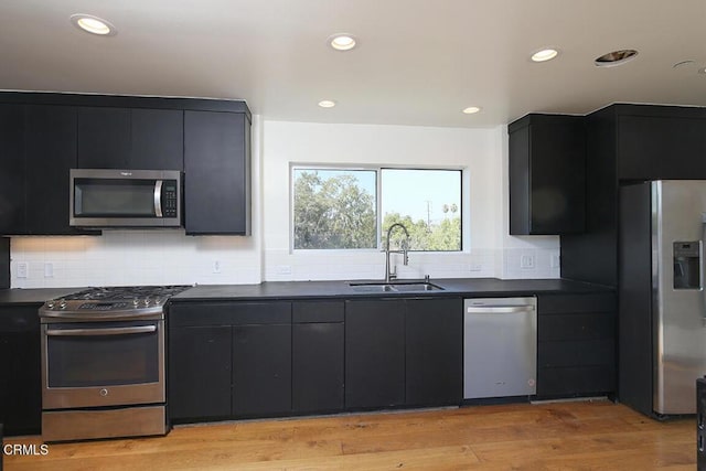 kitchen with appliances with stainless steel finishes, sink, light wood-type flooring, and decorative backsplash