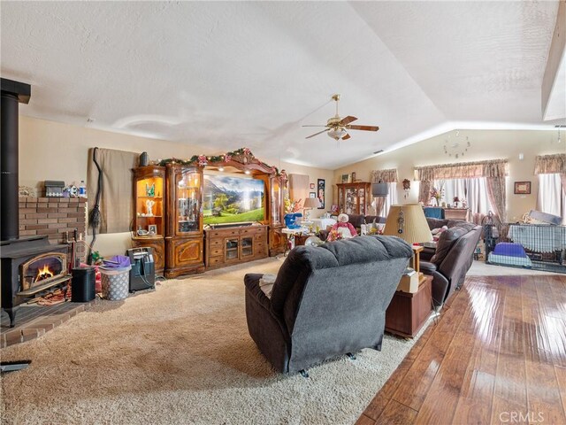 living room with vaulted ceiling, a wood stove, hardwood / wood-style flooring, ceiling fan, and a textured ceiling