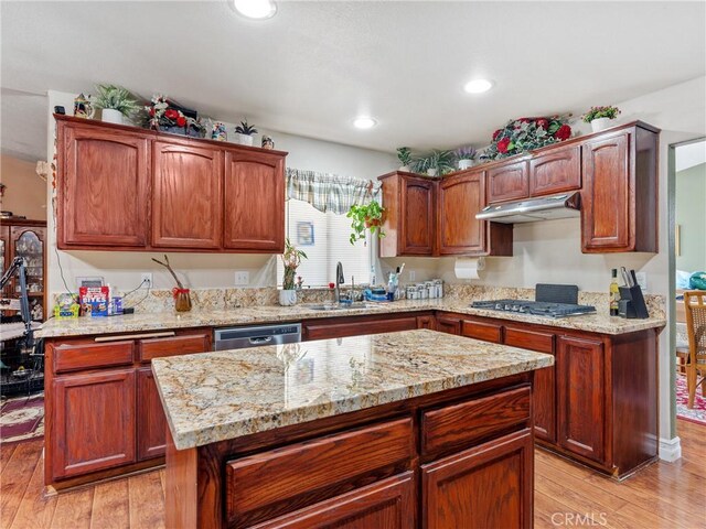 kitchen with sink, light wood-type flooring, light stone countertops, and a kitchen island